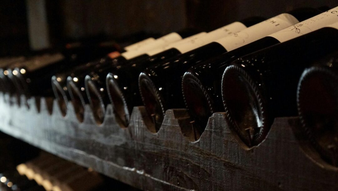A dimly lit wine cellar showcasing rows of wine bottles on rustic wooden shelves, creating a classic and elegant atmosphere.